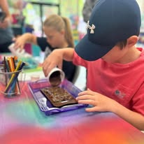 A boy pouring melted chocolate into a mold at a bright activity table