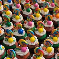 Rows of cupcakes topped with rainbow swirl lollipops, gumballs, and gummy candy
