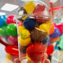 A clear cup packed with colorful gumballs and chocolate candies